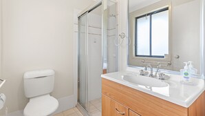 A bathroom with a toilet, a shower enclosure, and a sink with a mirror above it. - Fingal Sands 10A - Fingal Bay (Fingal Bay)