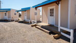 Uma fileira de pequenas cabanas térreas, com design semelhante, cada uma com varanda frontal e porta com janelas.