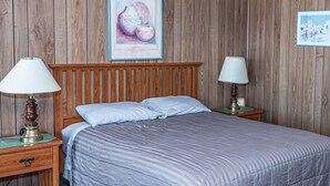 Quarto com cabeceira de madeira, duas luminárias de apoio, cama com manta listrada e quadro na parede.