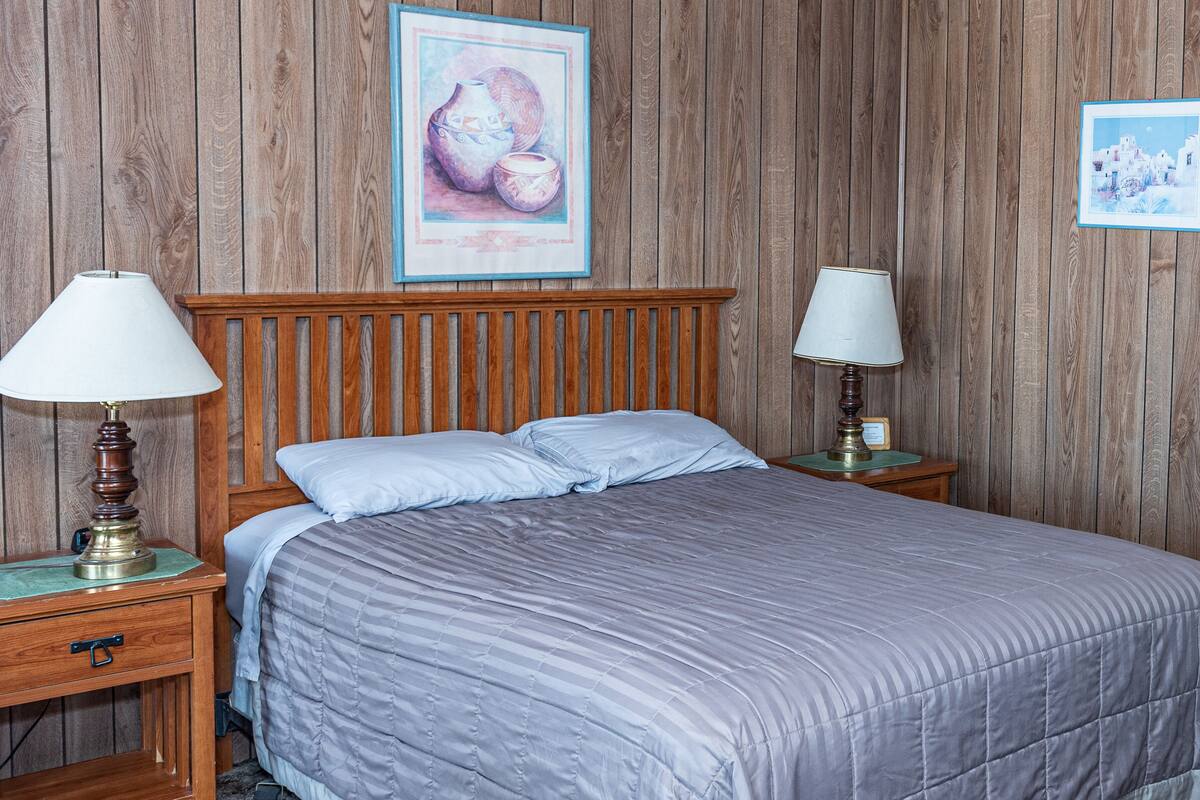 A bedroom with a wooden headboard, two bedside lamps, a bed with a striped blanket, and a framed picture on the wall.