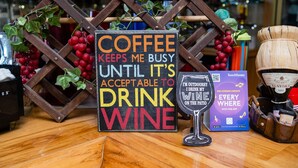 Um sinal com uma mensagem bem-humorada sobre café e vinho, uma taça de vinho e uma caixa do aplicativo TouchTunes.