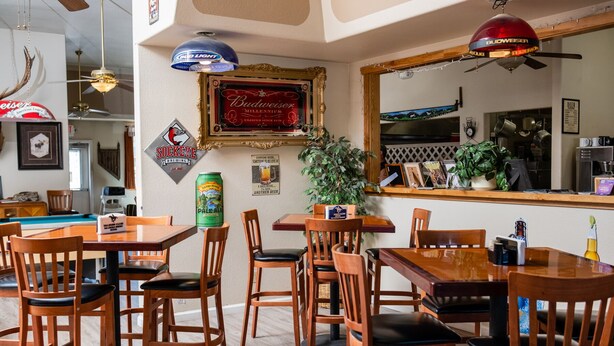 Interior de restaurante com mesas e cadeiras de madeira, uma torneira de cerveja e um quadro com um letreiro na parede.