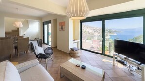 A spacious living area with a large window offering a view of the sea, a flat-screen TV, and a dining area with wicker furniture. - villa with great seaview (Schinias)