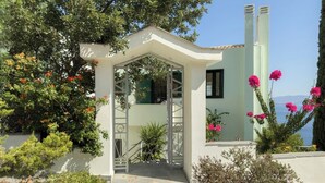 A white building with a covered entrance, stone steps, and surrounding greenery. - villa with great seaview (Schinias)
