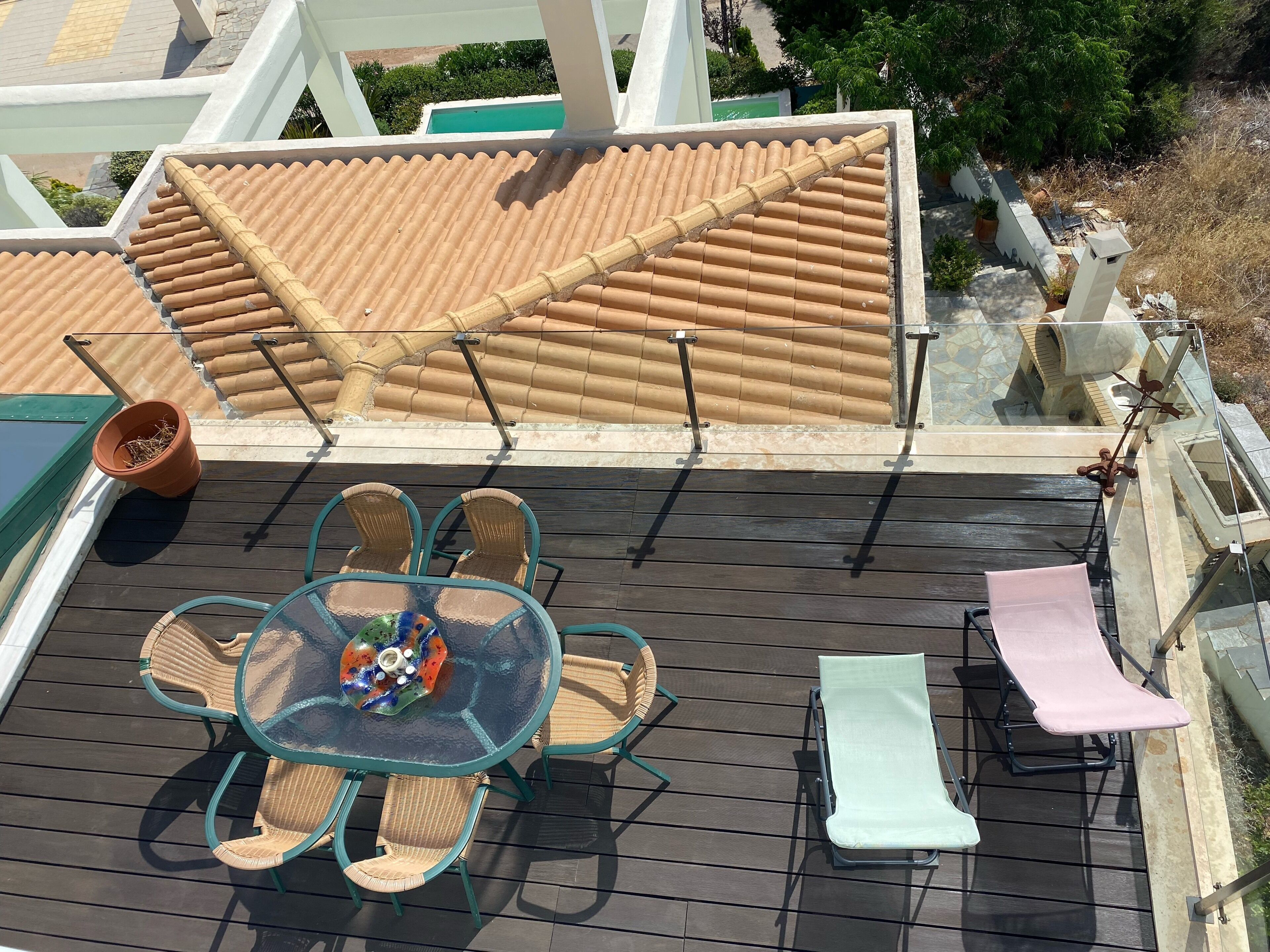 Eine Dachterrasse mit Ziegeldach, einem Glastisch mit Stühlen und einer Liege.