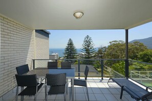 Een balkon met een tafel en stoelen, een bankje, en uitzicht op zee en bomen.