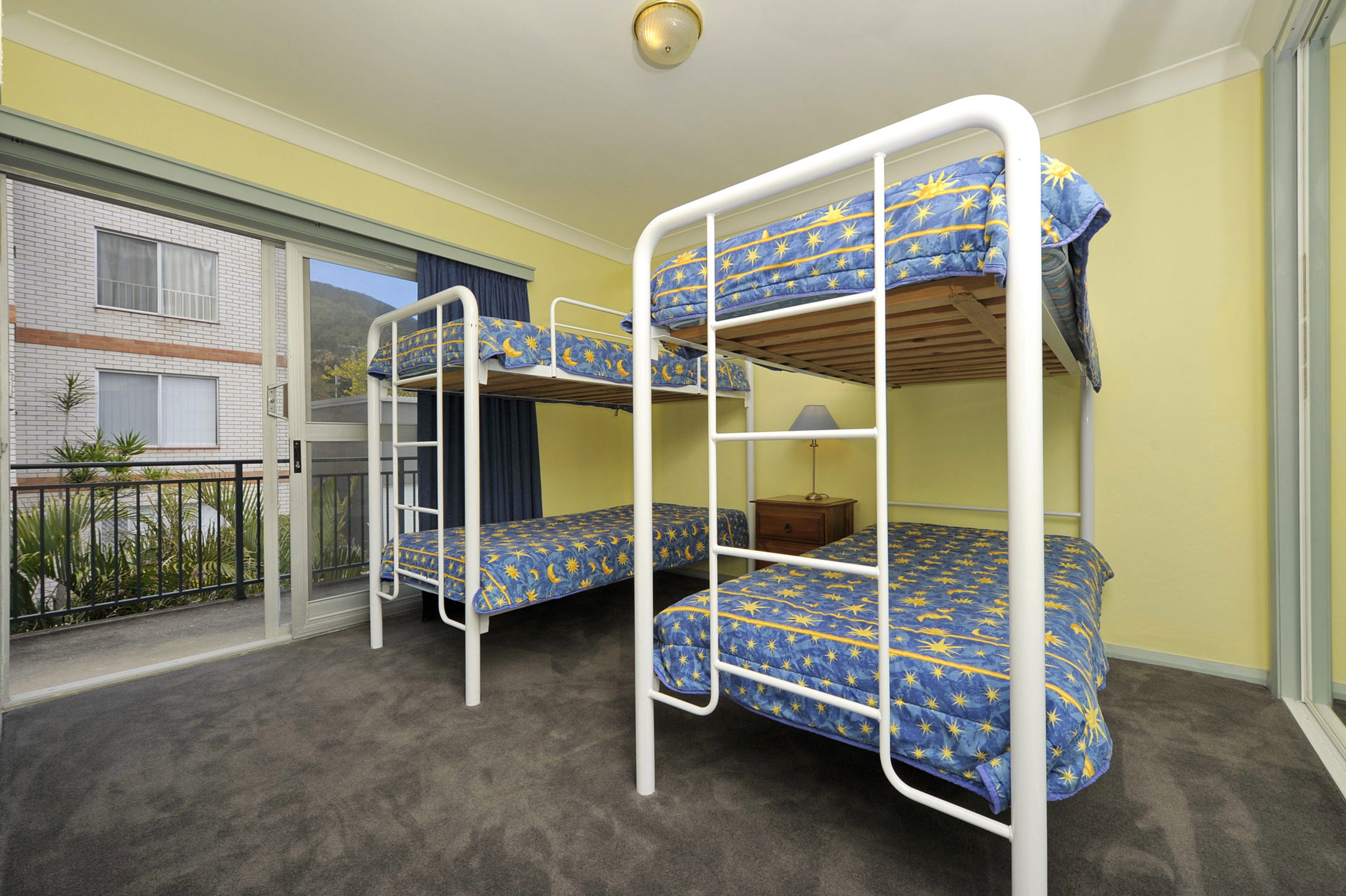 A room with bunk beds, a small table, and a window with a view of a building.
