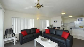 Una sala de estar con dos sofás negros, una mesa de centro blanca y un ventilador de techo.