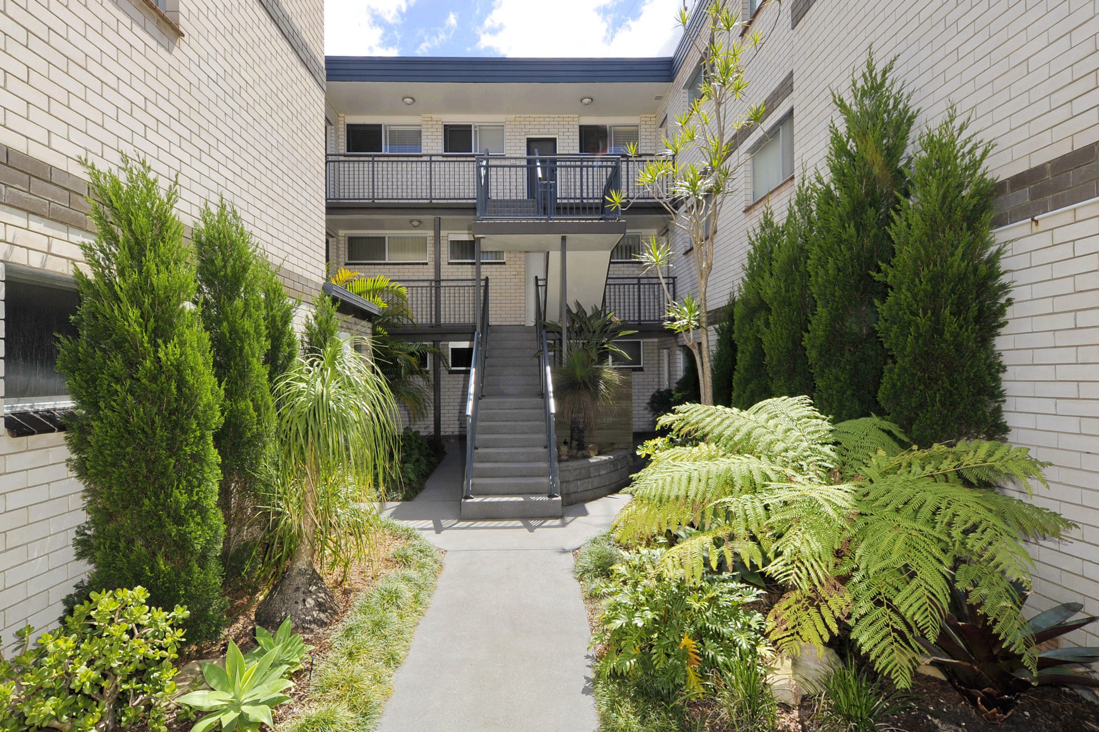 A multi-level building with a central staircase, surrounded by various plants and shrubs.