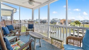 A covered outdoor area with wooden furniture, a ceiling fan, and a view of a residential area and water body. - Oceanfront Heaven's Anchor in Holden Beach, 3BR, 2BA, perfect for family fun! (Holden Beach)