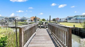 A wooden boardwalk leading to a waterfront area with buildings in the background. - Oceanfront Heaven's Anchor in Holden Beach, 3BR, 2BA, perfect for family fun! (Holden Beach)
