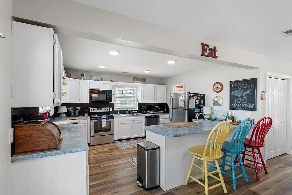 A modern kitchen with white cabinets, a central island, and colorful chairs.