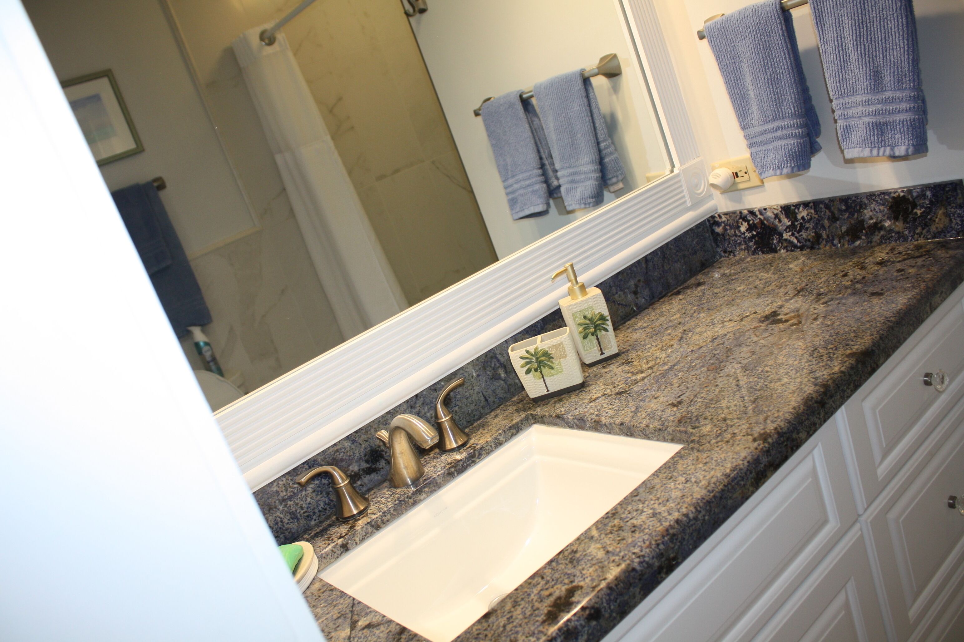 Une salle de bain avec un comptoir en granit, un lavabo blanc, des robinets dorés et un miroir au-dessus du lavabo.