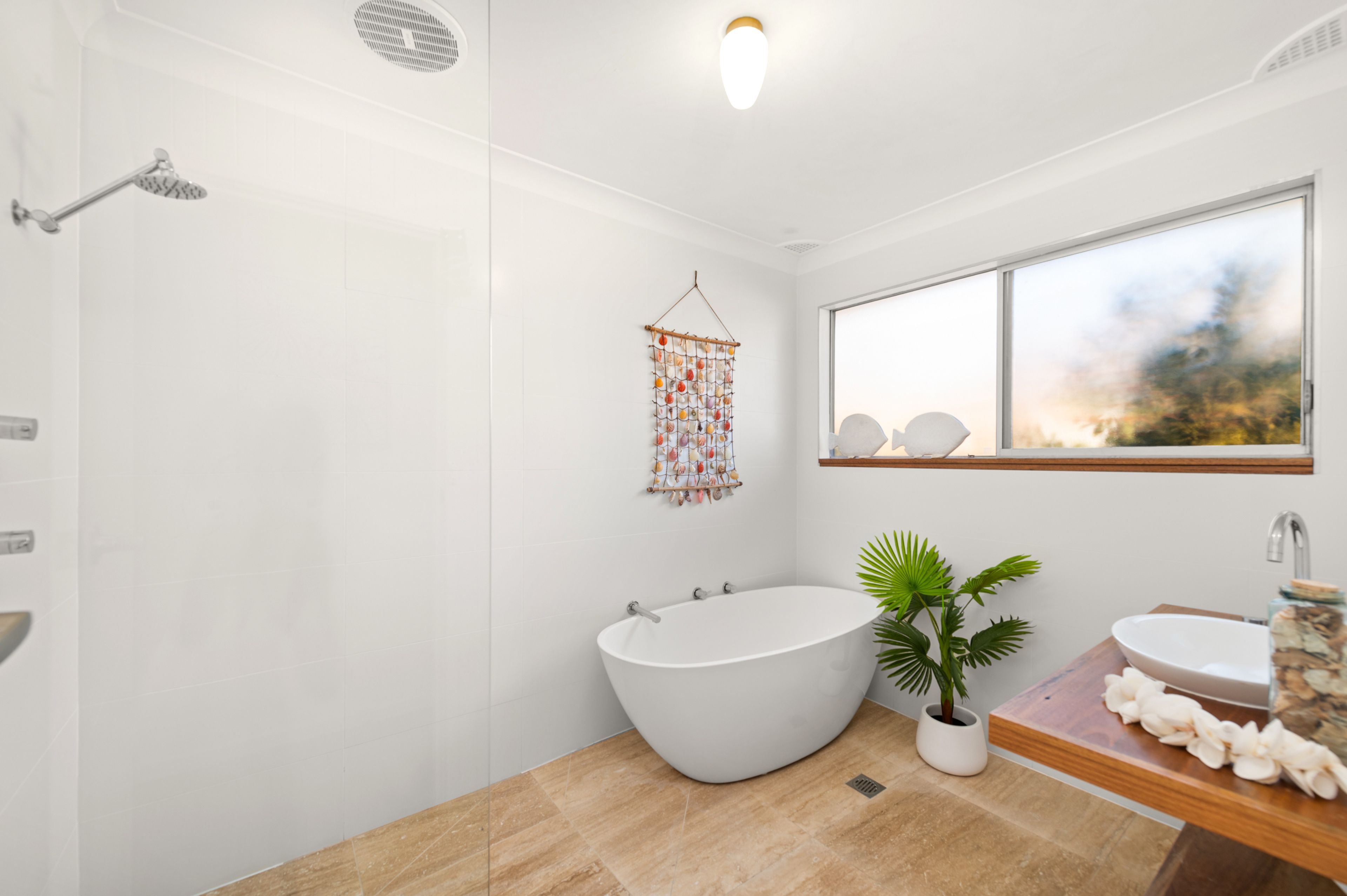 A modern bathroom with a freestanding bathtub, a window with a view, and a decorative wall hanging.