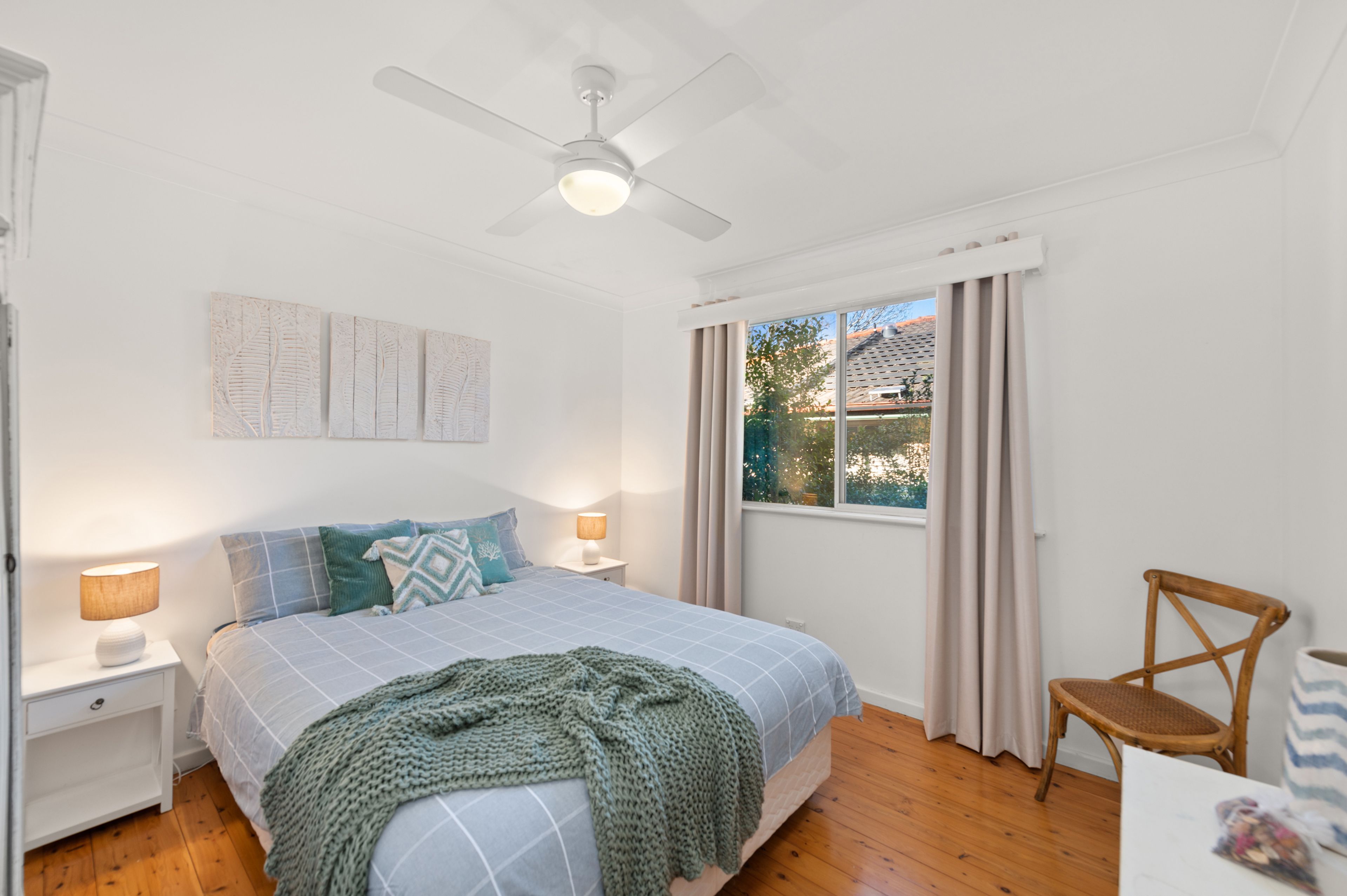 A bedroom with a bed, nightstands, a lamp, a ceiling fan, a window with curtains, and a chair.