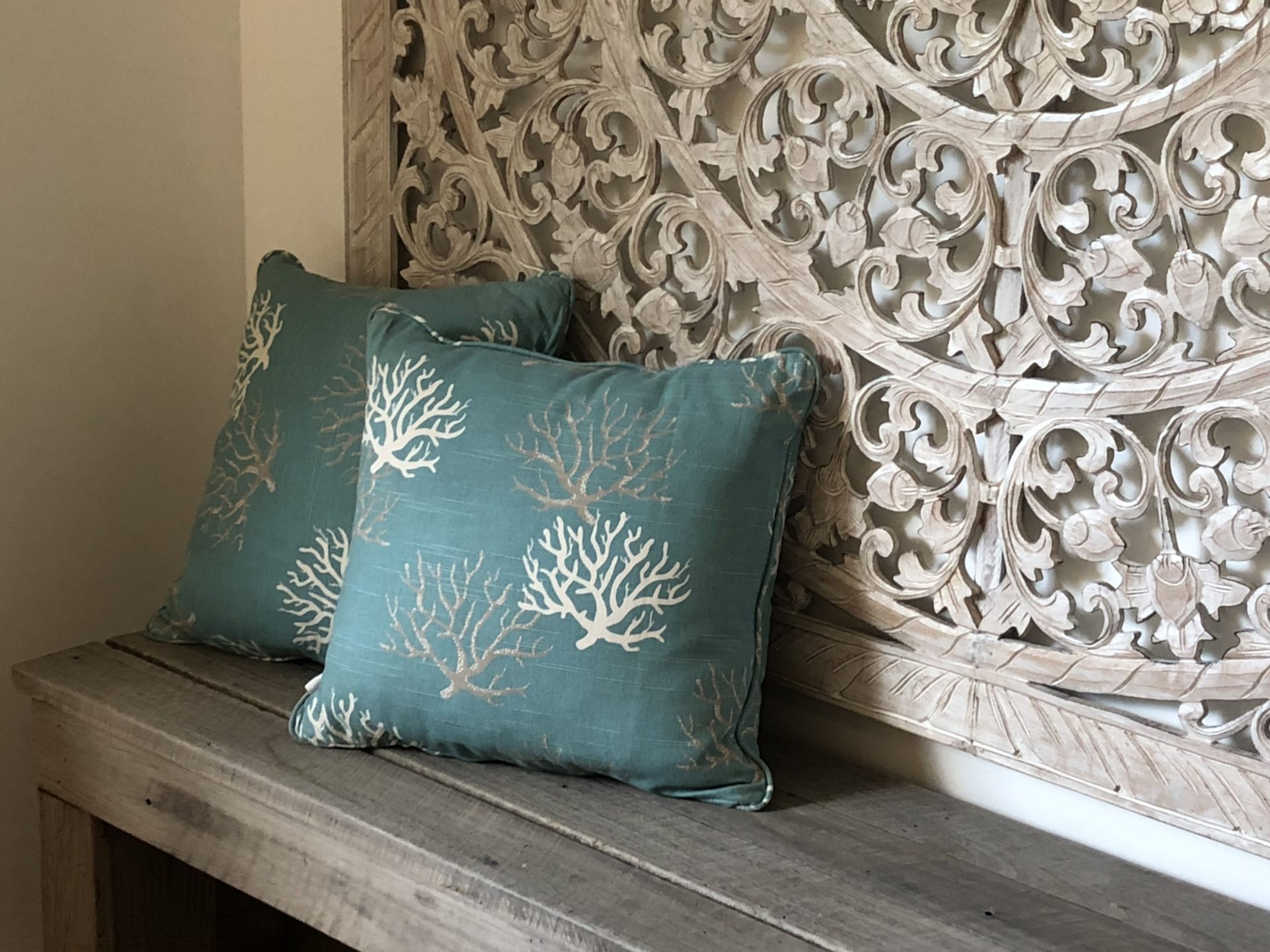 A bench with two teal pillows featuring white tree patterns, positioned against a wall with ornate, carved white paneling.