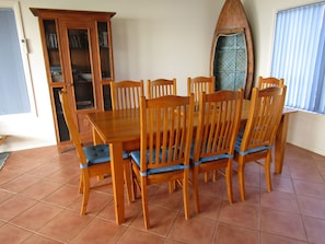 A dining area with a wooden table and chairs, a cabinet, and a surfboard decoration. - Woody's Beach House ~ Beautiful Sea Views, Great Position, Off Peak Special! (Point Turton)