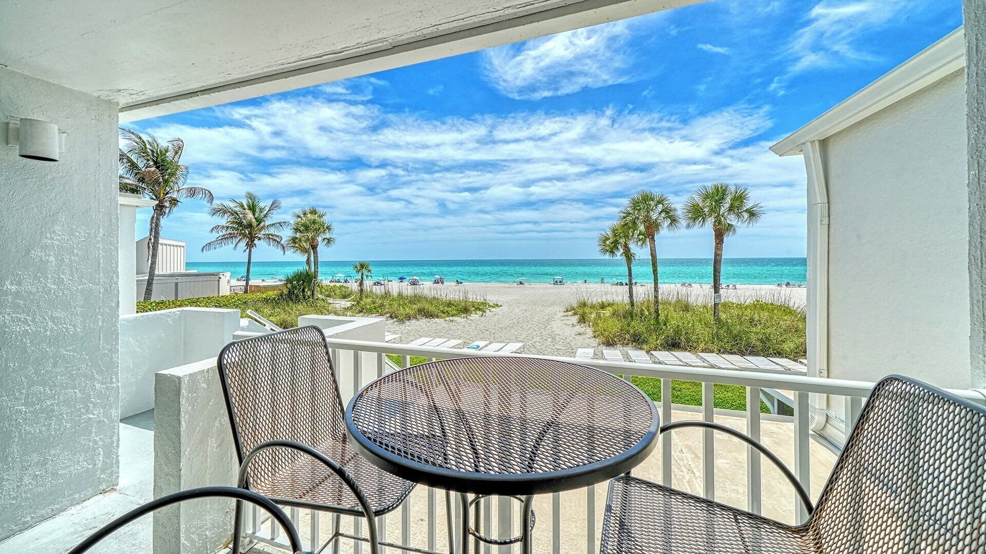 A balcony with a view of a beach, featuring a table and chairs.