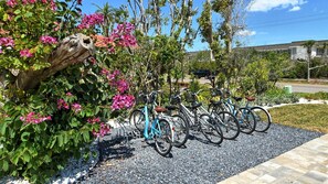 Bicycles are secured to a metal rack in a well-maintained area with interlocking pavers and lush greenery.