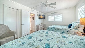 A bedroom with two beds, a ceiling fan, a dresser, and a television on the wall.