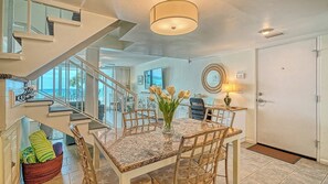 Uma sala de estar espaçosa com uma mesa de jantar, cadeiras, um vaso de flores, uma escada e vista para o oceano.