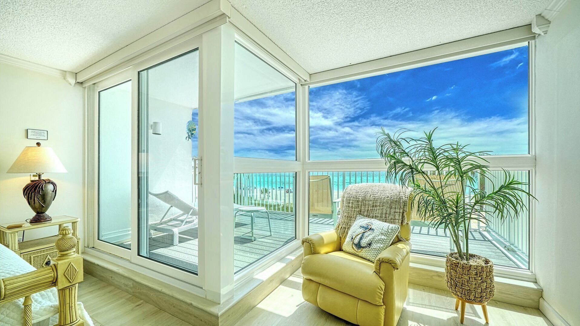 A room with a large window, a yellow armchair, a lamp, and a potted plant.