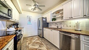 A kitchen with white cabinets, a stainless steel refrigerator, a stove, and a ceiling fan. - LaPlaya 204D-Beach-lovers paradise! (Longboat Key)