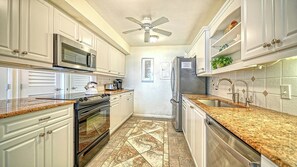 A kitchen with white cabinetry, a stainless steel refrigerator, a microwave, a stove, and a ceiling fan. - LaPlaya 204D-Beach-lovers paradise! (Longboat Key)