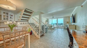 Uma sala de estar ampla com escada, cozinha com bancada de mármore e vista para o oceano.