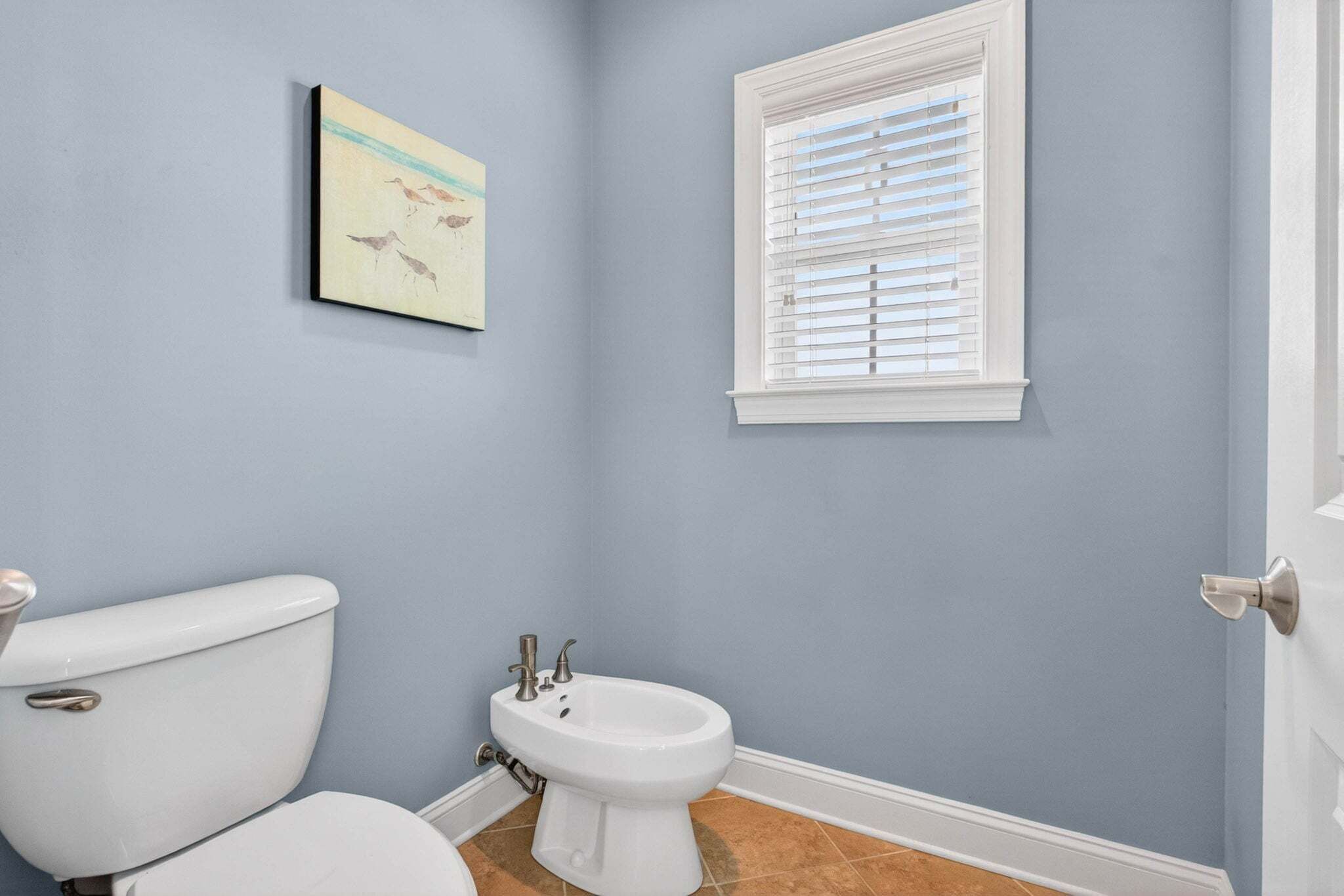 A bathroom with a toilet, bidet, and a window with blinds.