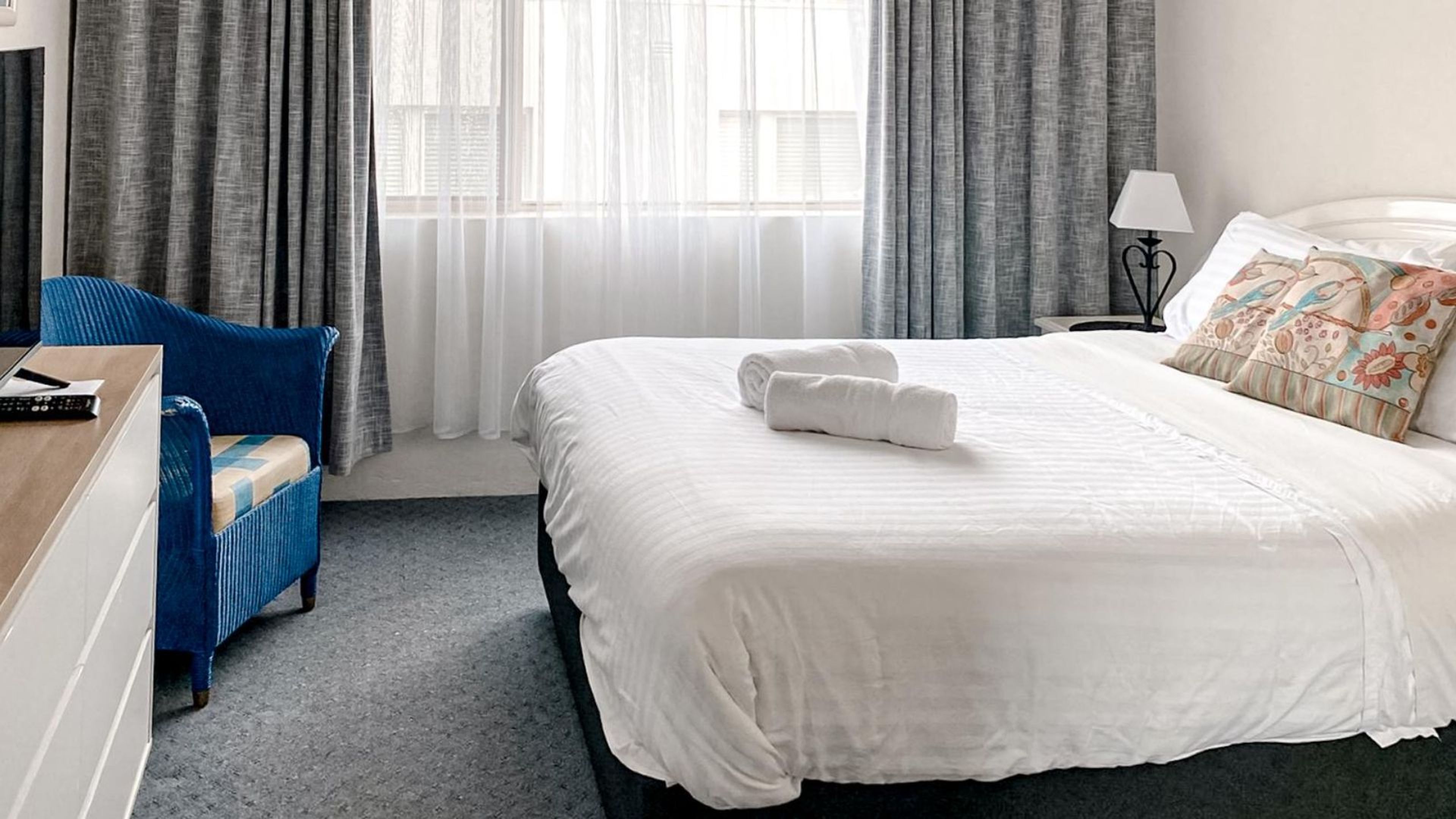 Ein Hotelzimmer mit Bett, Stuhl, Schreibtisch und einem fenster mit Vorhängen.