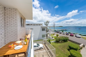 A balcony with a table set for dining, overlooking a marina with boats and a clear sky. - Del Rae 8 Beachfront Apartment Shoal Bay (Shoal Bay)