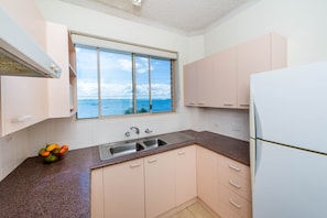 A kitchen with a view of the sea, a sink, and a refrigerator. - Del Rae 8 Beachfront Apartment Shoal Bay (Shoal Bay)
