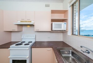 A compact kitchen with a stove, microwave, and a window with a view of the sea.