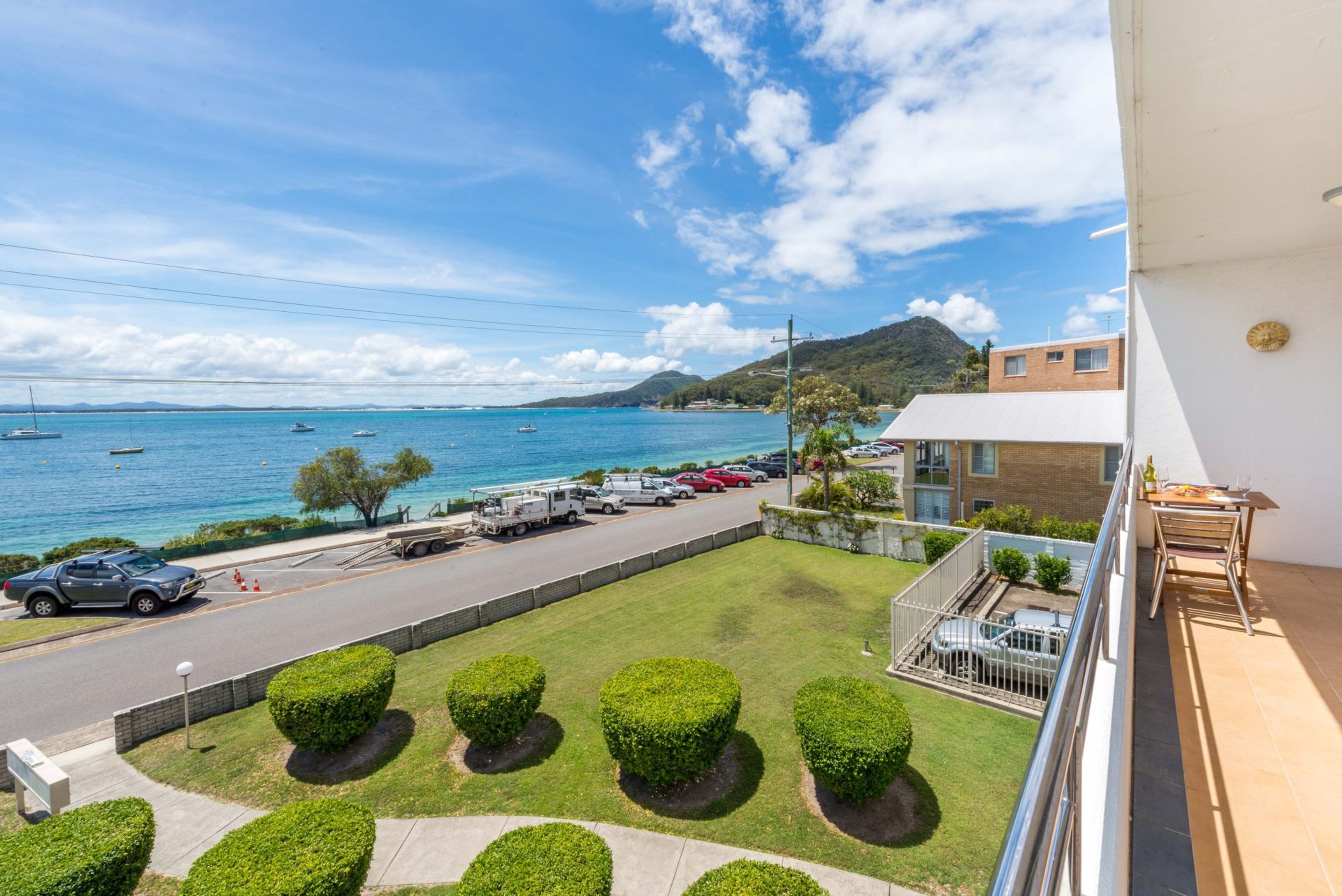 A coastal view with a road, parked cars, and a building with a balcony.