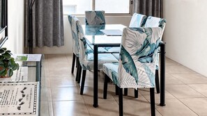 A dining area with a table and chairs, a potted plant, and a window with curtains. - Del Rae 8 Beachfront Apartment Shoal Bay (Shoal Bay)