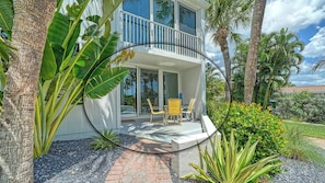 A two-story house with a balcony, surrounded by tropical plants and palm trees.