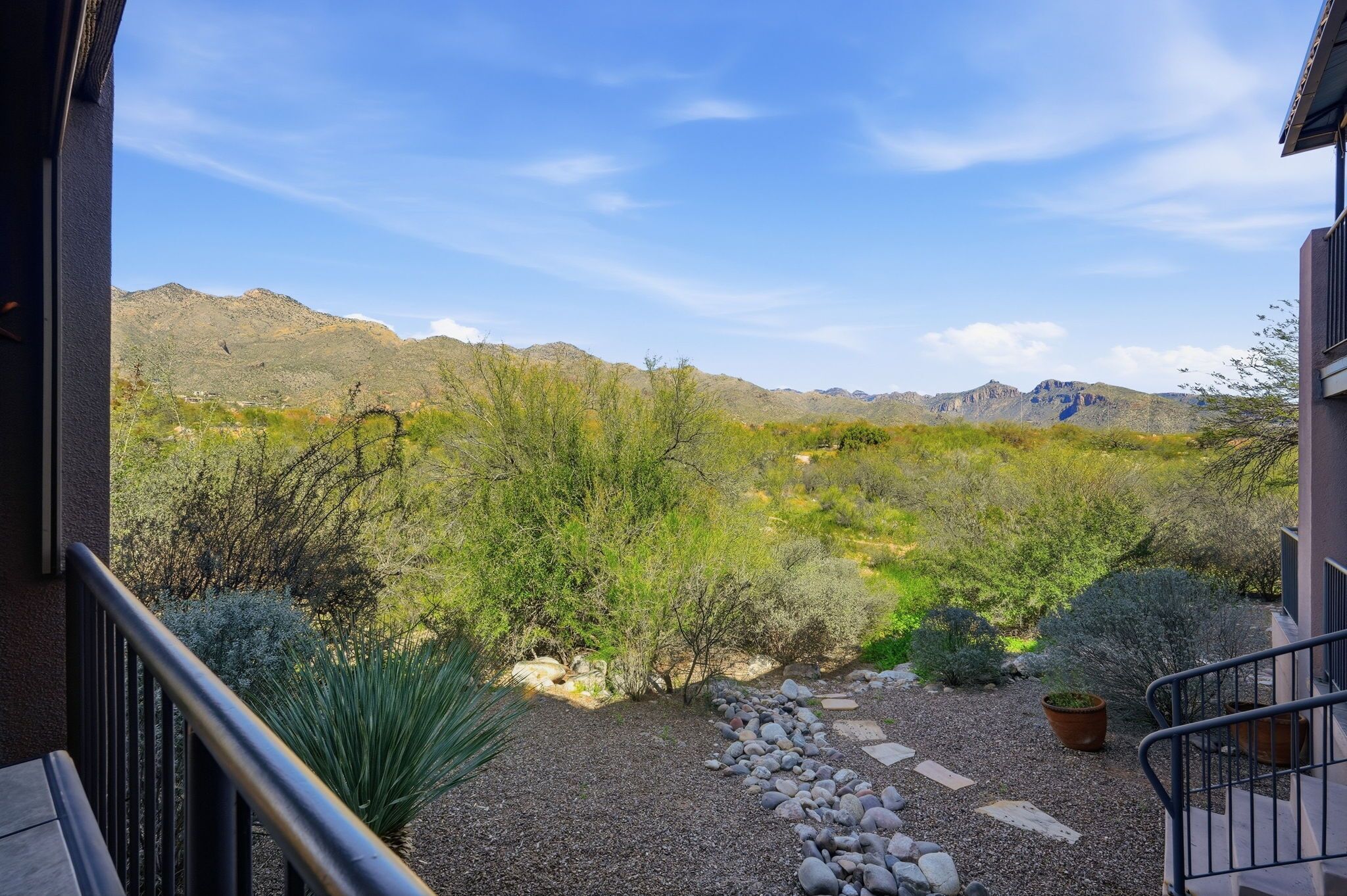 Une vue depuis un balcon donnant sur un jardin aménagé, avec différents arbustes et une chaîne de montagnes au loin.
