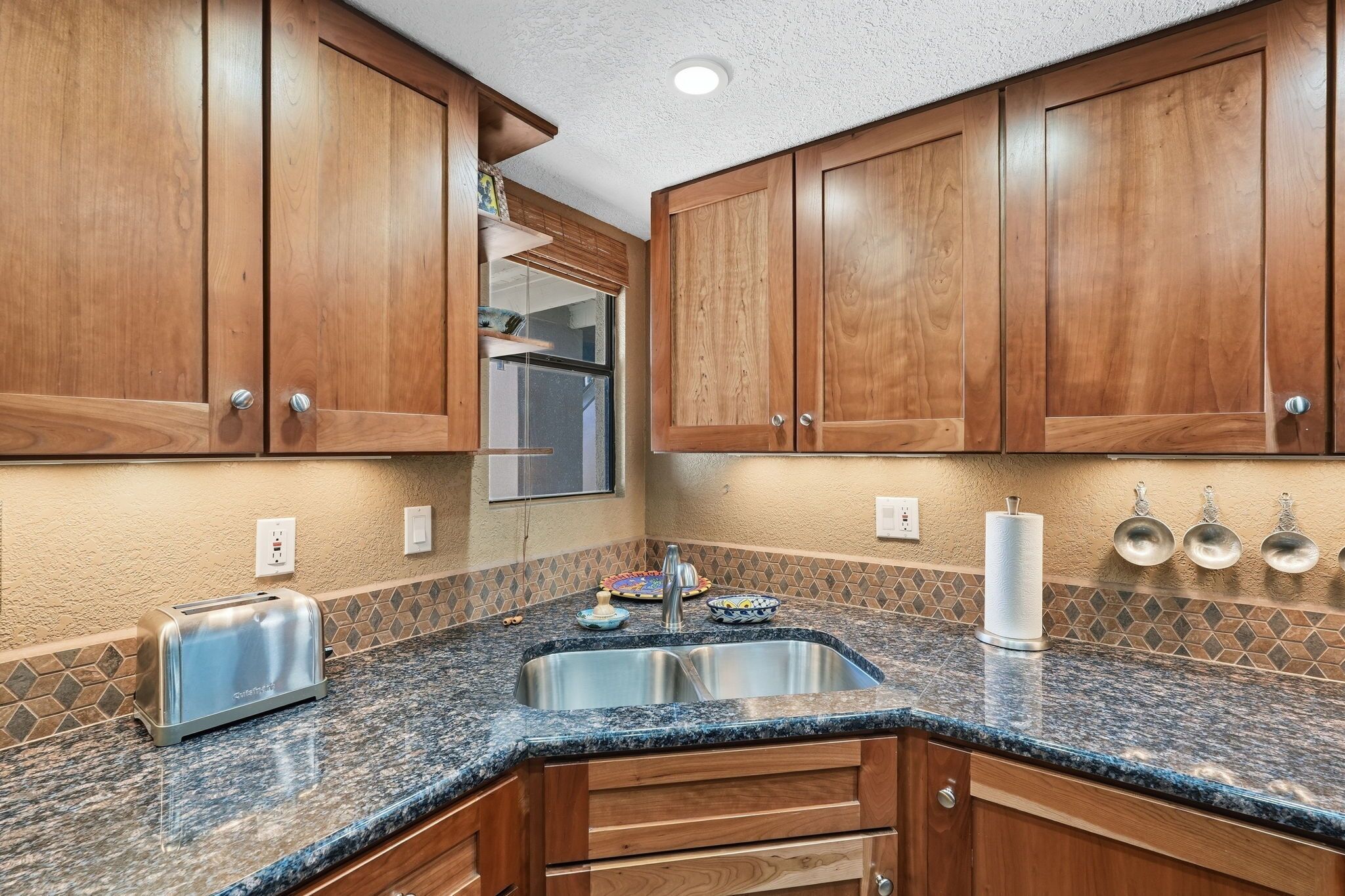 A kitchen with wooden cabinets, a granite countertop, a stainless steel sink, and a toaster.