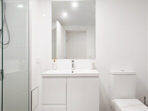 Een moderne badkamer met een glazen douchecabine, een wit wastafelmeubel met een spiegel erboven en een toilet.