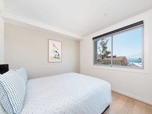 Een slaapkamer met een bed, een ingelijst kunstwerk aan de muur en een raam met uitzicht op de zee.