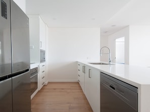 A modern kitchen with stainless steel appliances, white cabinetry, and a wooden floor. - The Shoal 210 Modern Apartment in Shoal Bay (Shoal Bay)