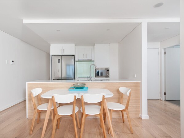 A modern kitchen with a central island, white cabinetry, and a stainless steel refrigerator. - The Shoal 210 Modern Apartment in Shoal Bay (Shoal Bay)