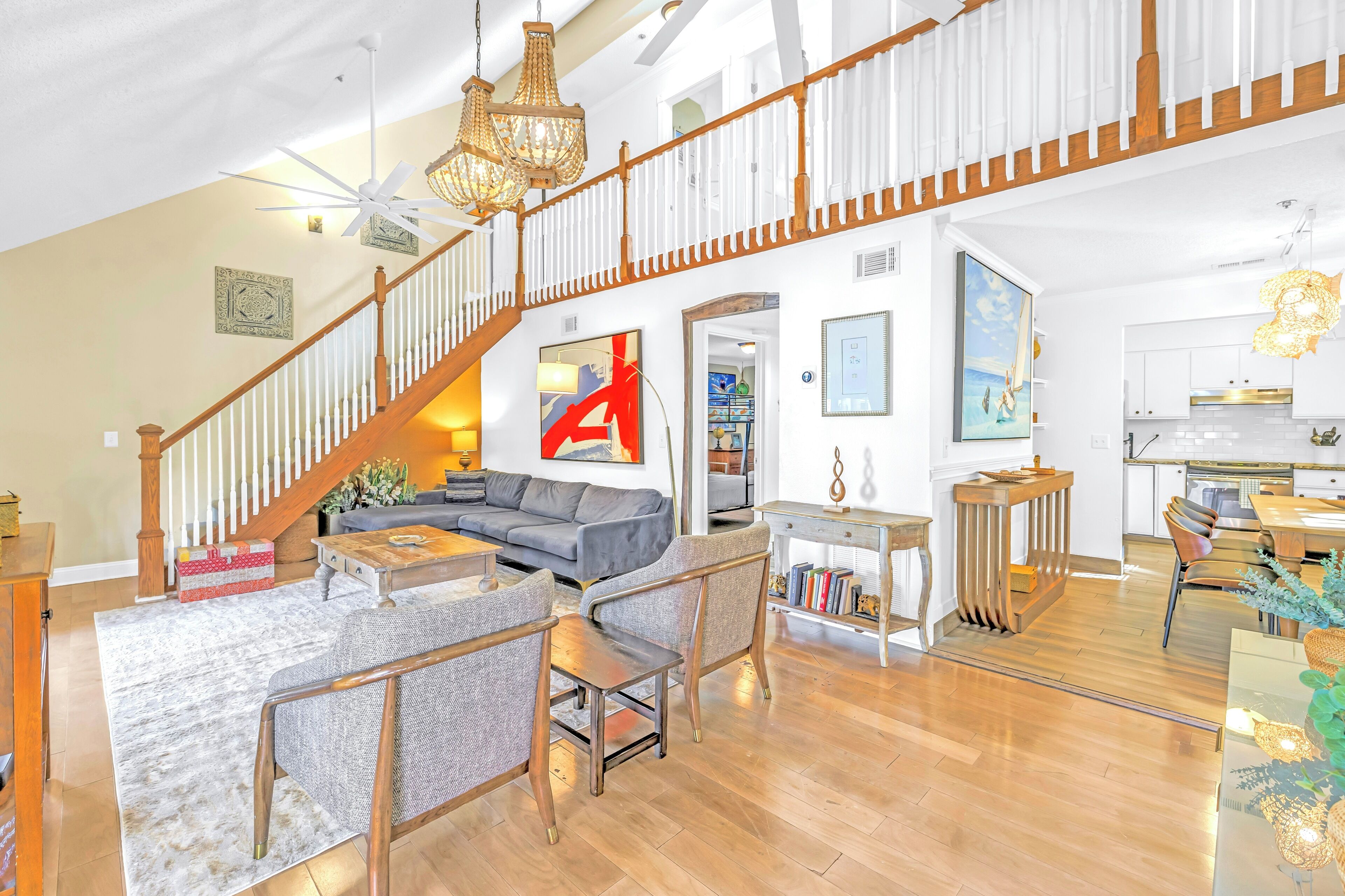 A spacious living area with a wooden staircase, a grey sofa, and a dining table.