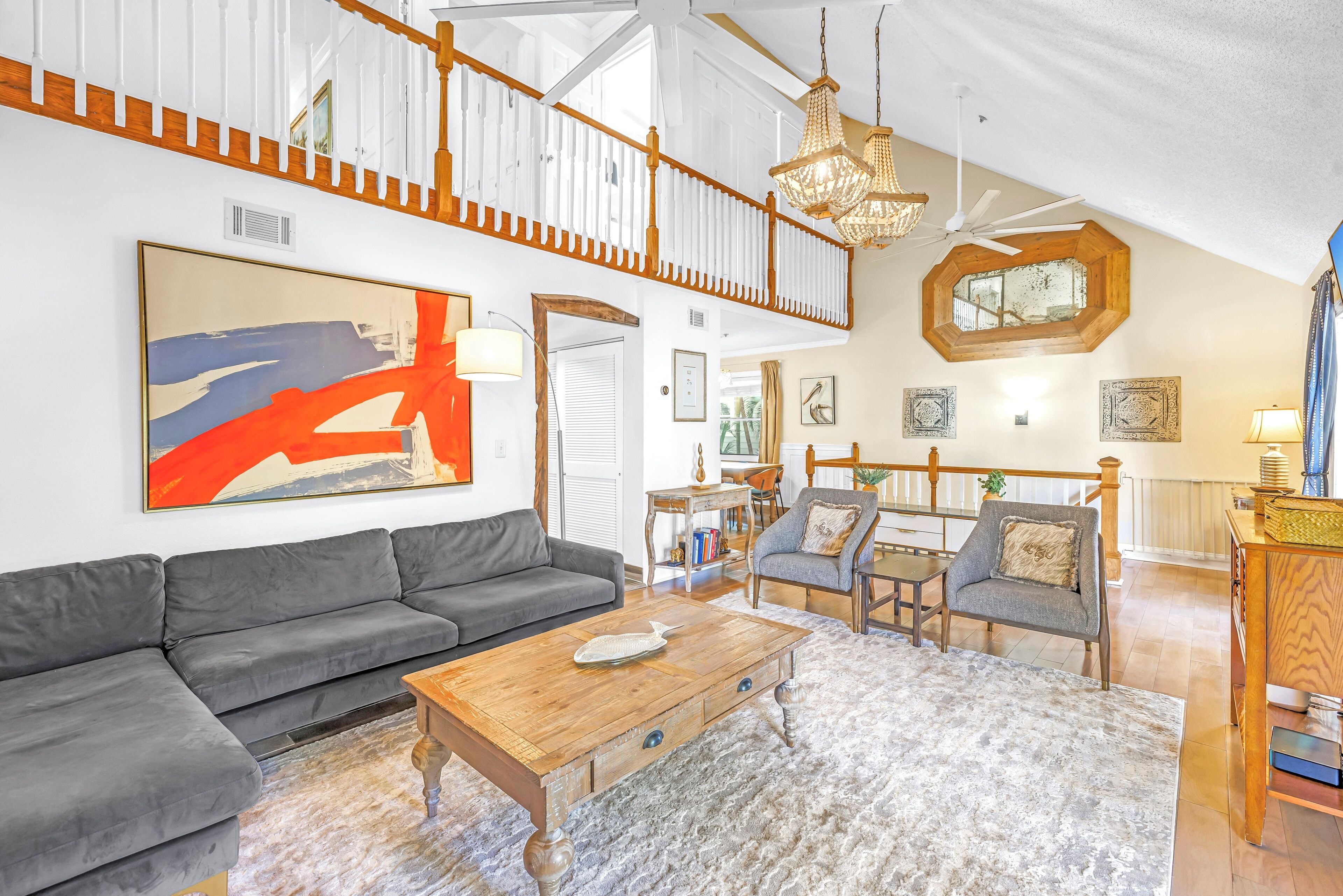 A spacious living room with a gray sectional sofa, a wooden coffee table, and a large abstract painting.