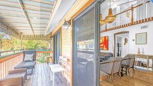 Eine überdachte Terrasse im Freien mit Rattanmöbeln, eine Schiebetür zu einem Innenbereich mit Esstisch und Stühlen.