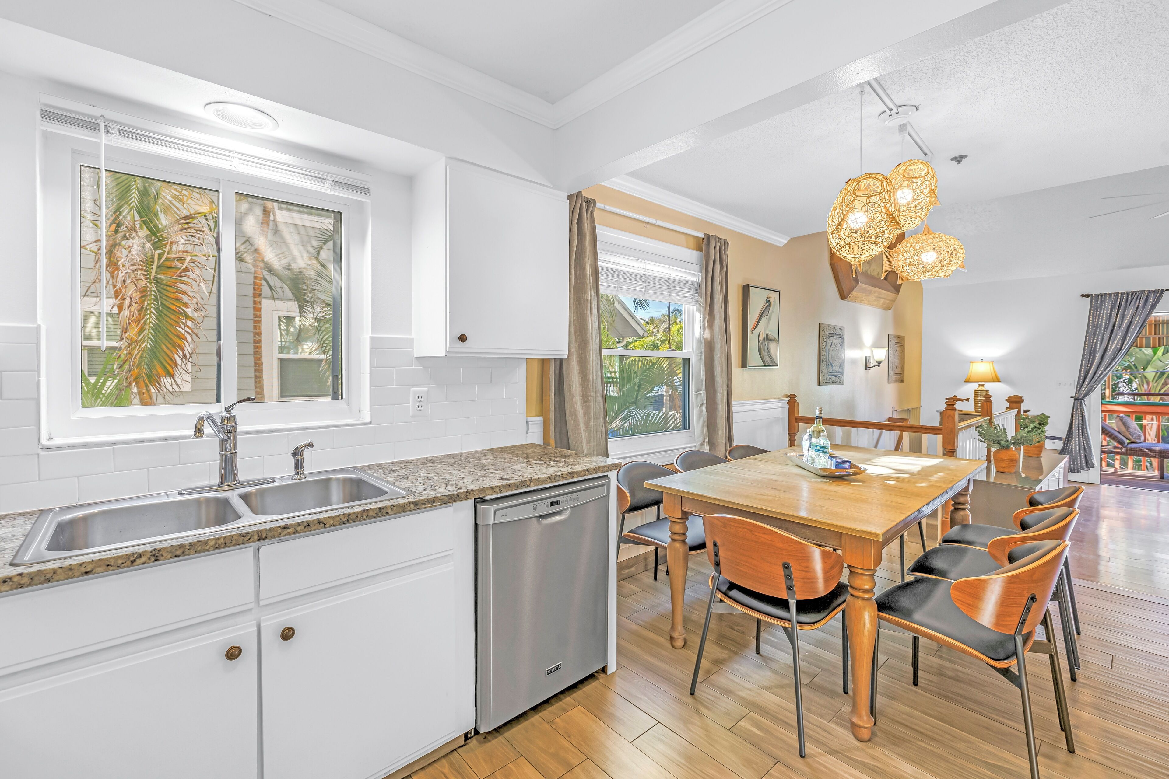 A modern kitchen with white cabinets, a dishwasher, a granite countertop, and a wooden dining table with chairs.