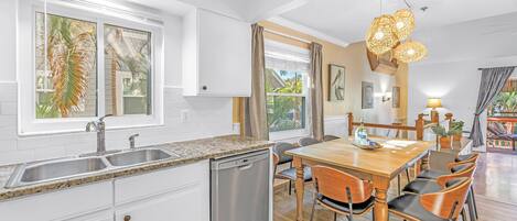 A modern kitchen with white cabinets, a dishwasher, a granite countertop, and a wooden dining table with chairs.
