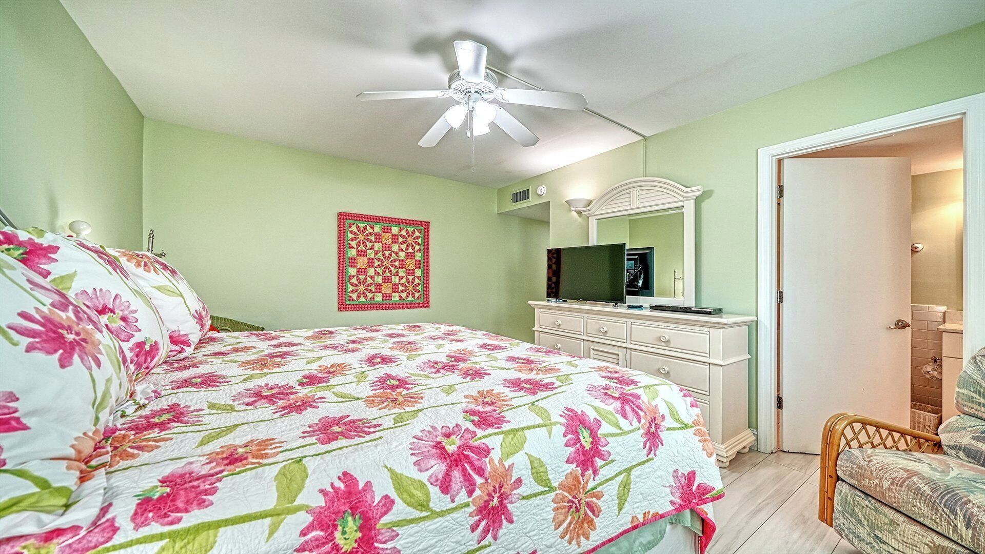 A bedroom with a bed, a dresser, a television, and a ceiling fan.