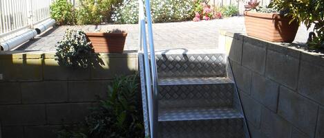 A set of outdoor stairs leading up to a rooftop area with potted plants and a white fence.